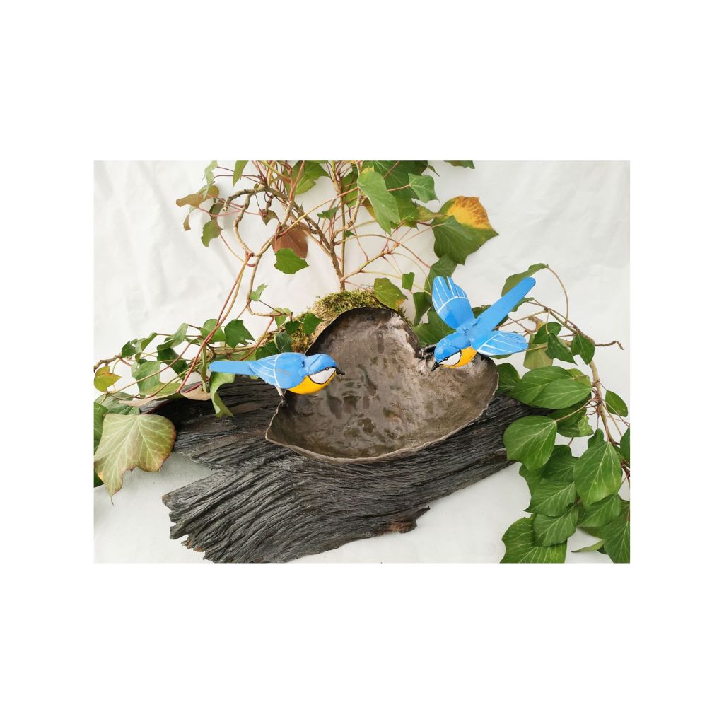 Bird bath recycled metal in the shape of a leaf with 2 bluetits birds, one with open wings & one with closed wings. Showing the leaf on a wood log.