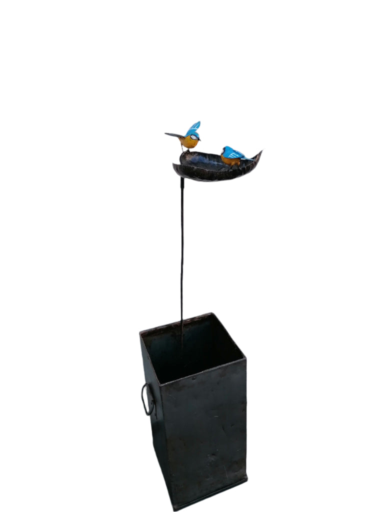Bird bath recycled metal in the shape of a leaf with 2 bluetits birds, one with open wings & one with closed wings. Showing the leaf on a stick in a zinc square planter.