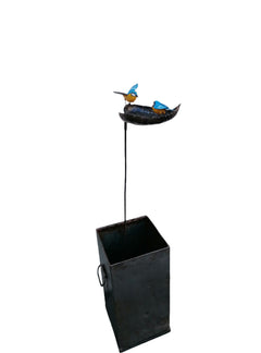 Bird bath recycled metal in the shape of a leaf with 2 bluetits birds, one with open wings & one with closed wings. Showing the leaf on a stick in a zinc square planter.