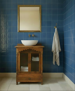 A small rustic wooden cabinet with two glass-front doors, a scalloped top frame, and a single drawer below, shown in a bathroom