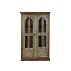 A rustic wooden cabinet with two doors, featuring distressed green and brown paint, vertical slat windows, and carved sunburst details on the lower panels.