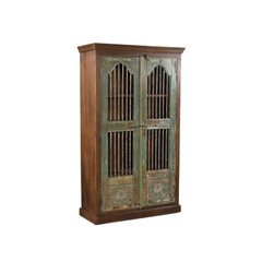 A rustic wooden cabinet with two doors featuring distressed green and brown painted panels, vertical metal bars, and carved sunburst details near the bottom, shown on a plain white background.