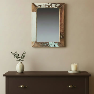 A rustic rectangular wall mirror with a distressed, peeling paint frame in brown, beige, and light blue tones, shown in a bedroom