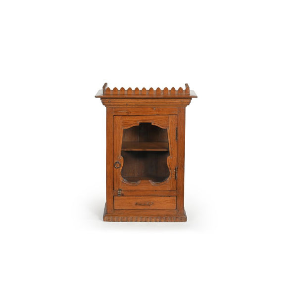 Light teak wood wall glass cabinet with an ornate glass door and a drawer at the bottom. The top of the cabinet has an ornate trim around.