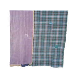 Two folded woven textiles hanging on a black metal stand against a rustic stone wall. The left textile is a solid dusty lavender-purple with a thin multicolor border.