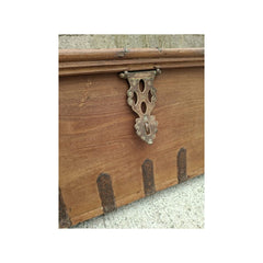 Close-up of a rustic wooden chest or box with an ornate metal latch and small metal feet, shown against a light textured background.