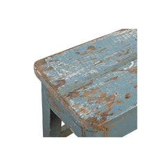 A close-up of a rustic wooden stool or table corner with distressed blue paint and exposed brown wood, shown on a plain white background.