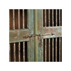 A close-up of a rustic decorative door with distressed teal-green paint, vertical slats, and an antique metal latch across the center.