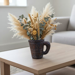 dark wood carved mug on a coffee table with dried flowers 